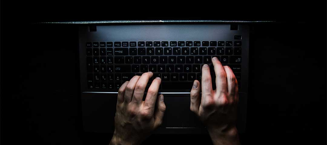 Image of hands hovering over keyboard illuminated by computer screen